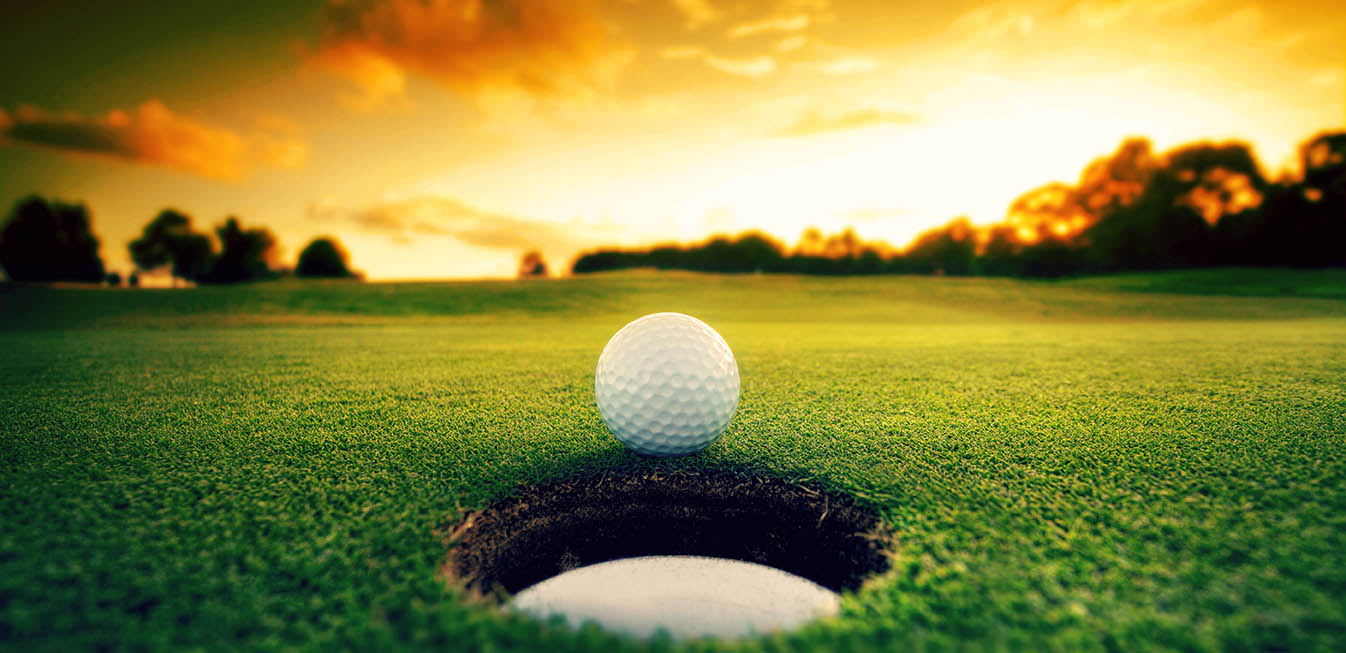 A golf ball rests on the edge of a hole at a luxurious resort's course, with a vibrant sunset sky in the background. The warm colors create a peaceful and scenic atmosphere, much like an evening on Minnesota’s Whitefish Chain of Lakes.